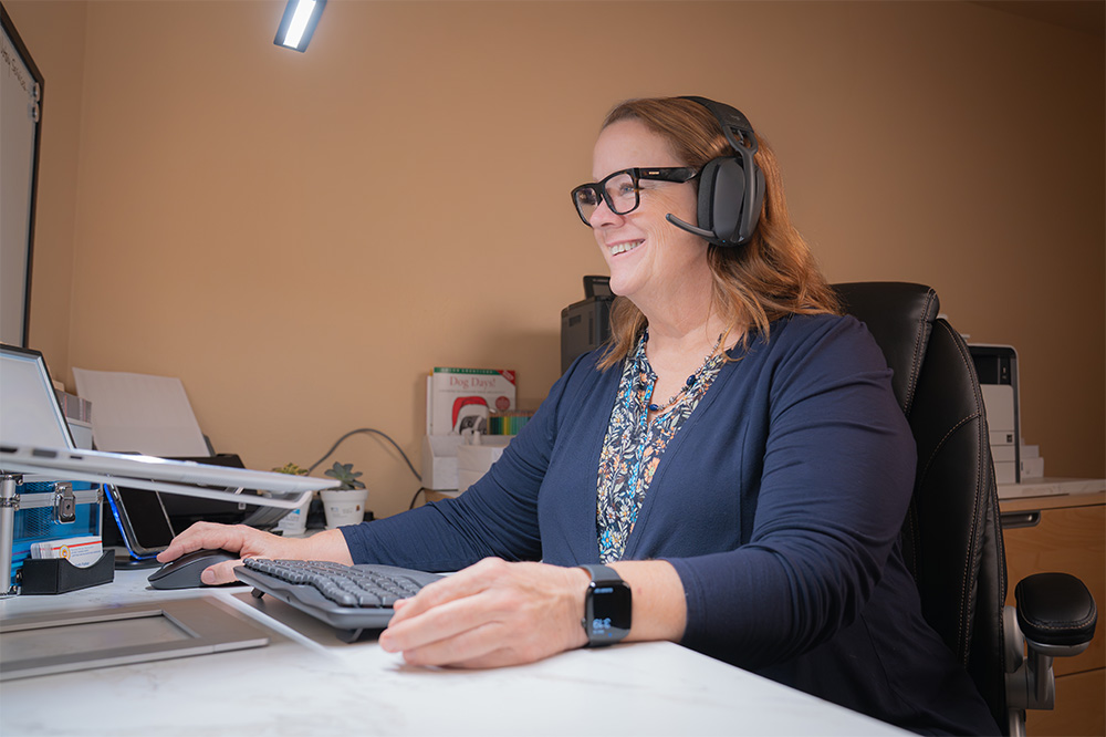 Meribeth Parker wearing a headset and working at her desk